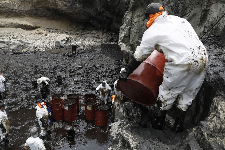 A cleanup crew works on a rocky shore that has been covered in spilled oil.