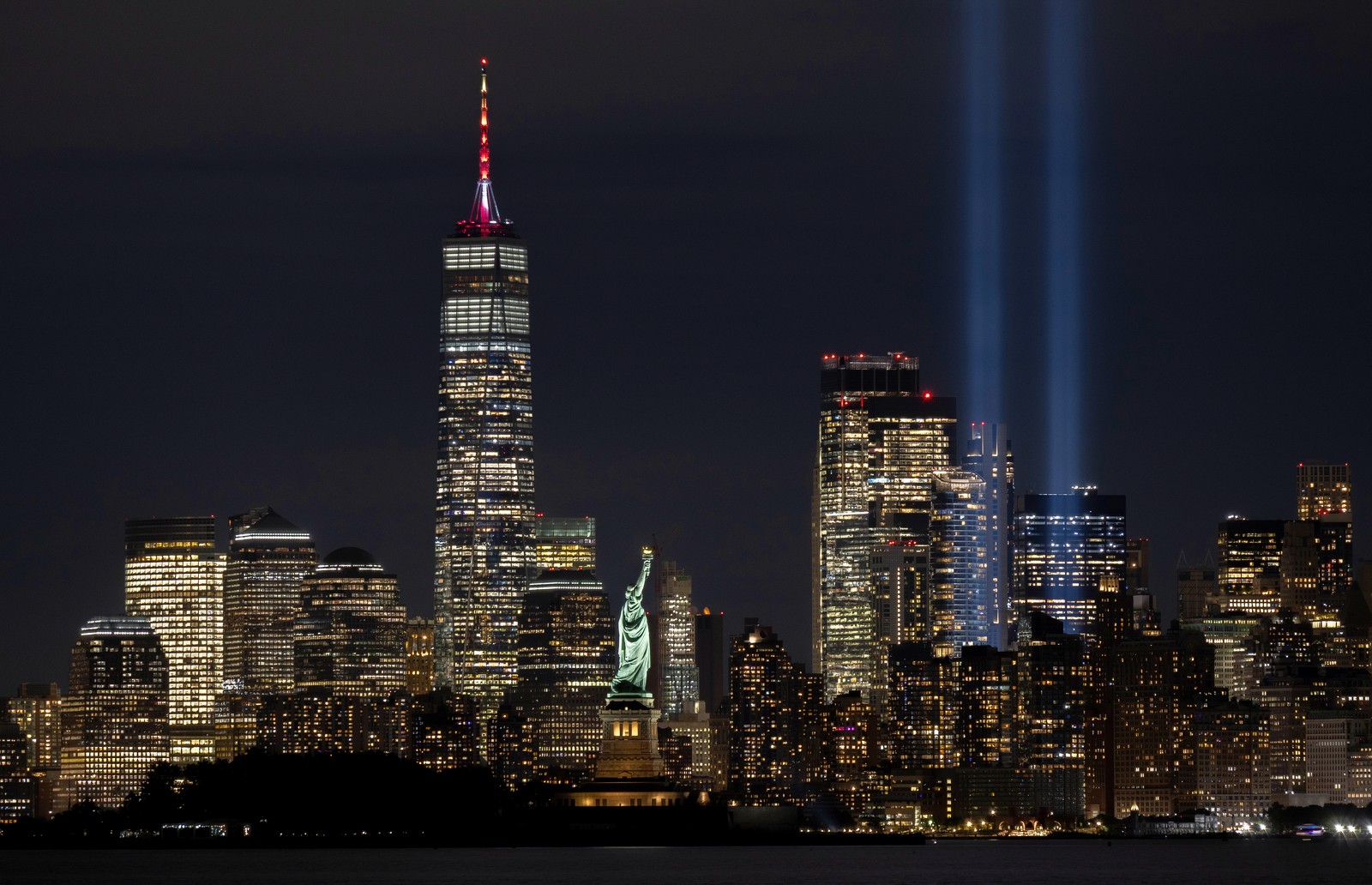A night view of the skyline of Manhattan, with two bright beams of light shining upward into the sky.