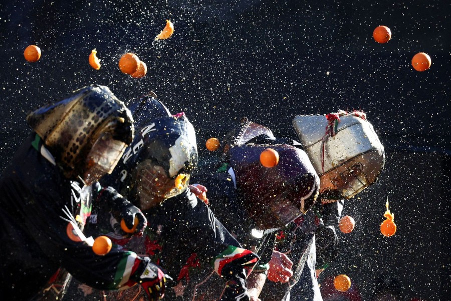 Several people wearing decorated protective gear are pelted with oranges.