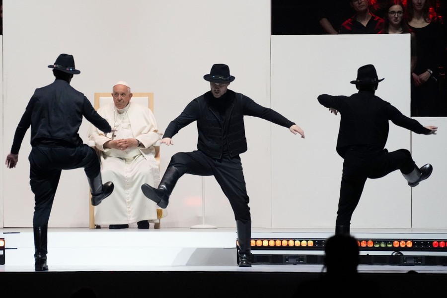 Three people in black suits, hats, and boots dance in front of the Pope.