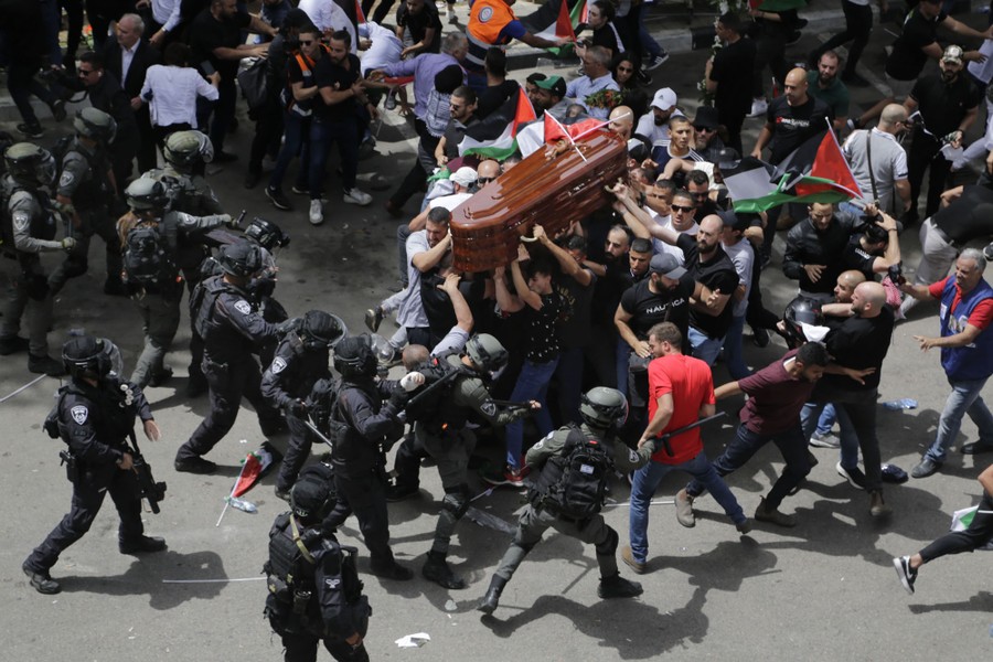 Riot-police officers beat a group of people who are carrying a coffin in a street.