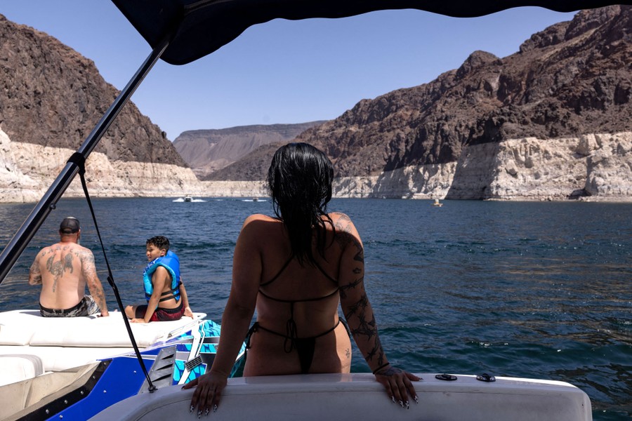 Several people are seen relaxing on boats floating in a reservoir surrounded by rocky cliffs.