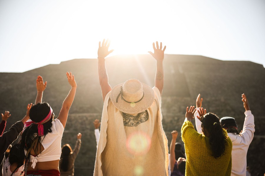 A group of people raise their arms toward the sun above a pyramid in Mexico.