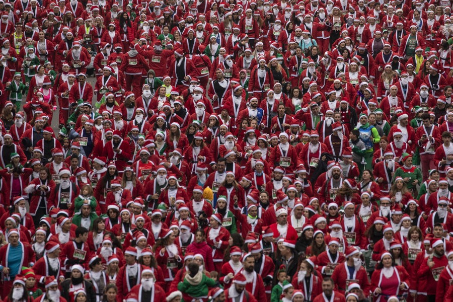Hundreds of people dressed as Santa run together down a wide street.