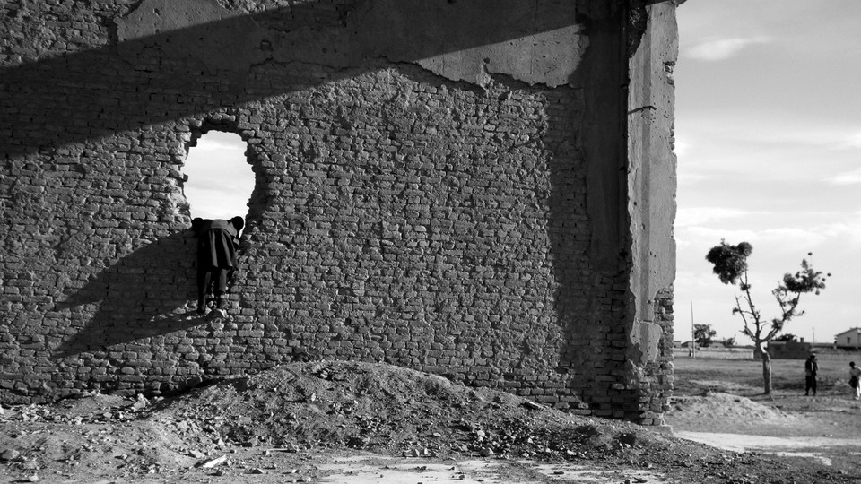 A black-and-white photo of a child playing in the ruins of a building in Afghanistan