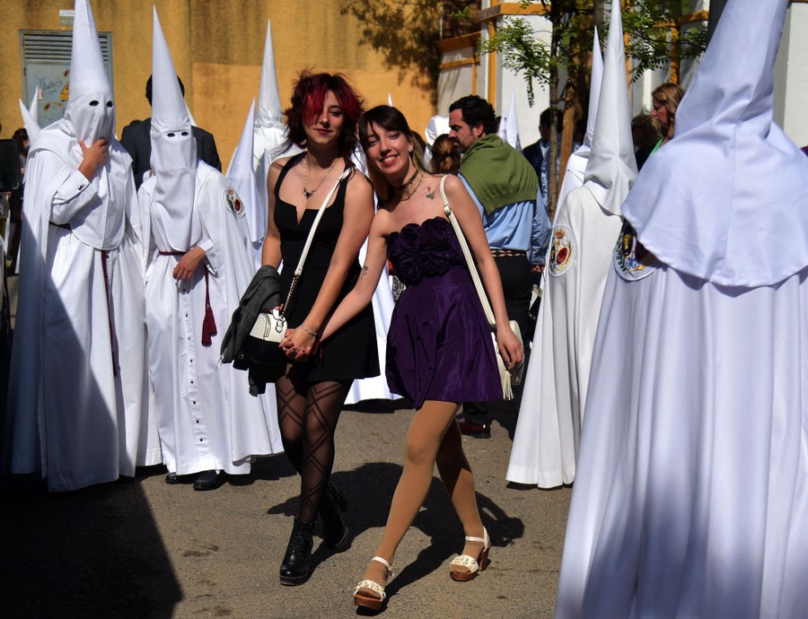 Two women walk among white-robed penitents in a courtyard.