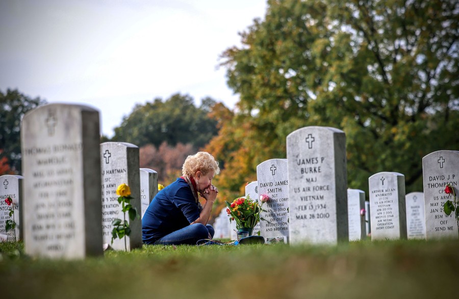 A woman visits her son's grave, among many headstones, in Arlington National Cemetery.