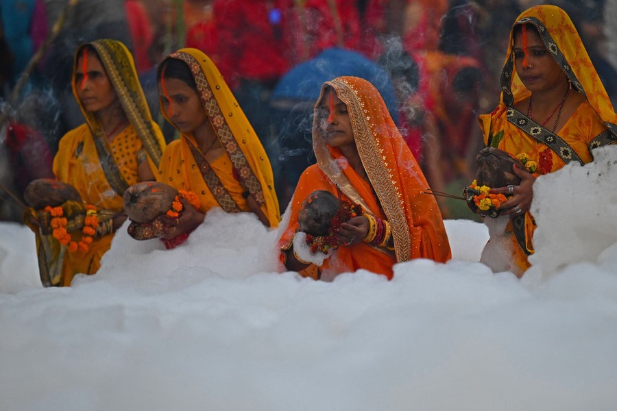 Several Hindu devotees are seen wearing saris while saying prayers in a foamy, polluted river.