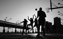 Black-and-white photo of silhouetted people playing basketball on an outdoor court