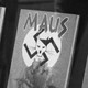 A black and white image of four 'Maus' books on a shelf. The cover depicts two mice huddled together under a swastika that bears the image of a cat drawn to look like Hitler