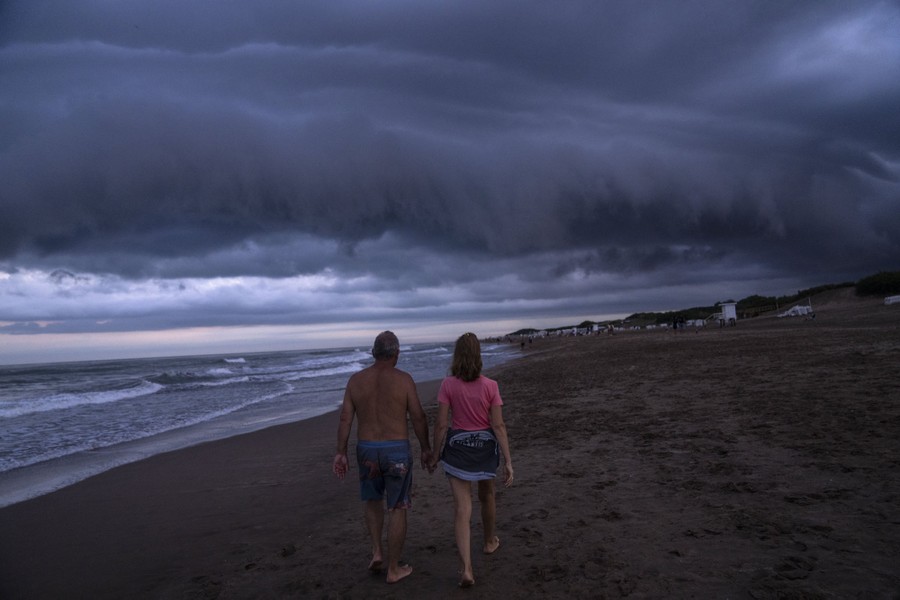 A couple walk on a beach during a rainy afternoon.