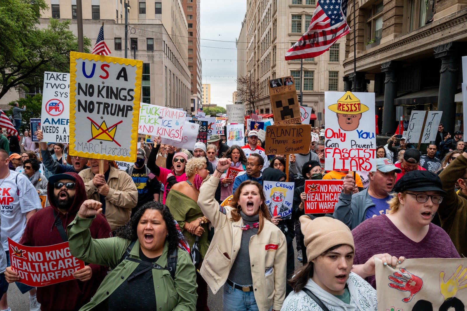 Protesters march through a Dallas city street, carrying anti-Trump protest signs.