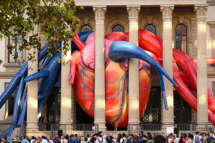 A giant inflatable heart sits wedged among tall columns at the entrance of a building.