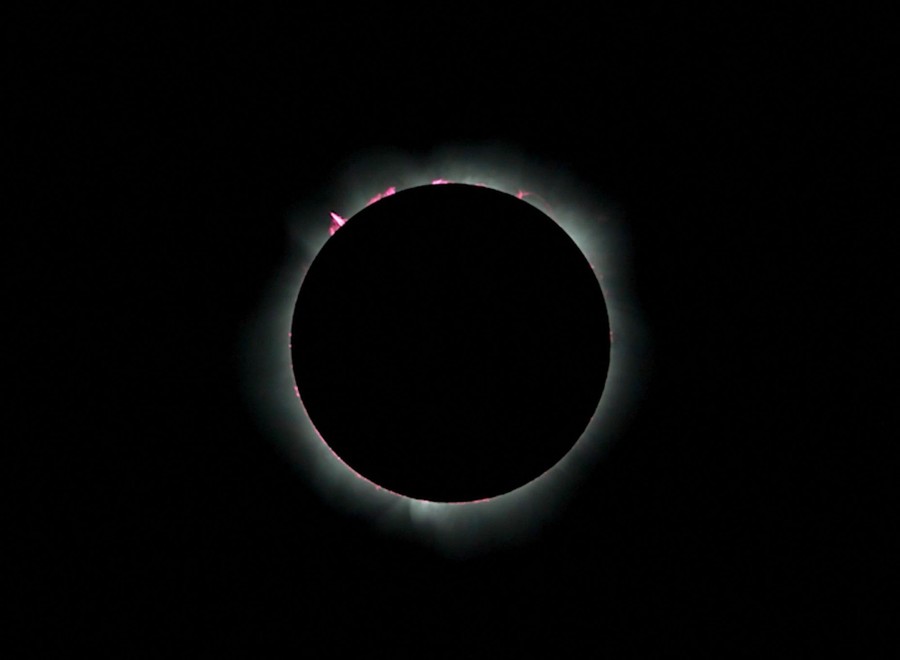A total eclipse, a dark image of the moon blocking the sun's light, except for a slender ring of jets and plumes visible at the edges.