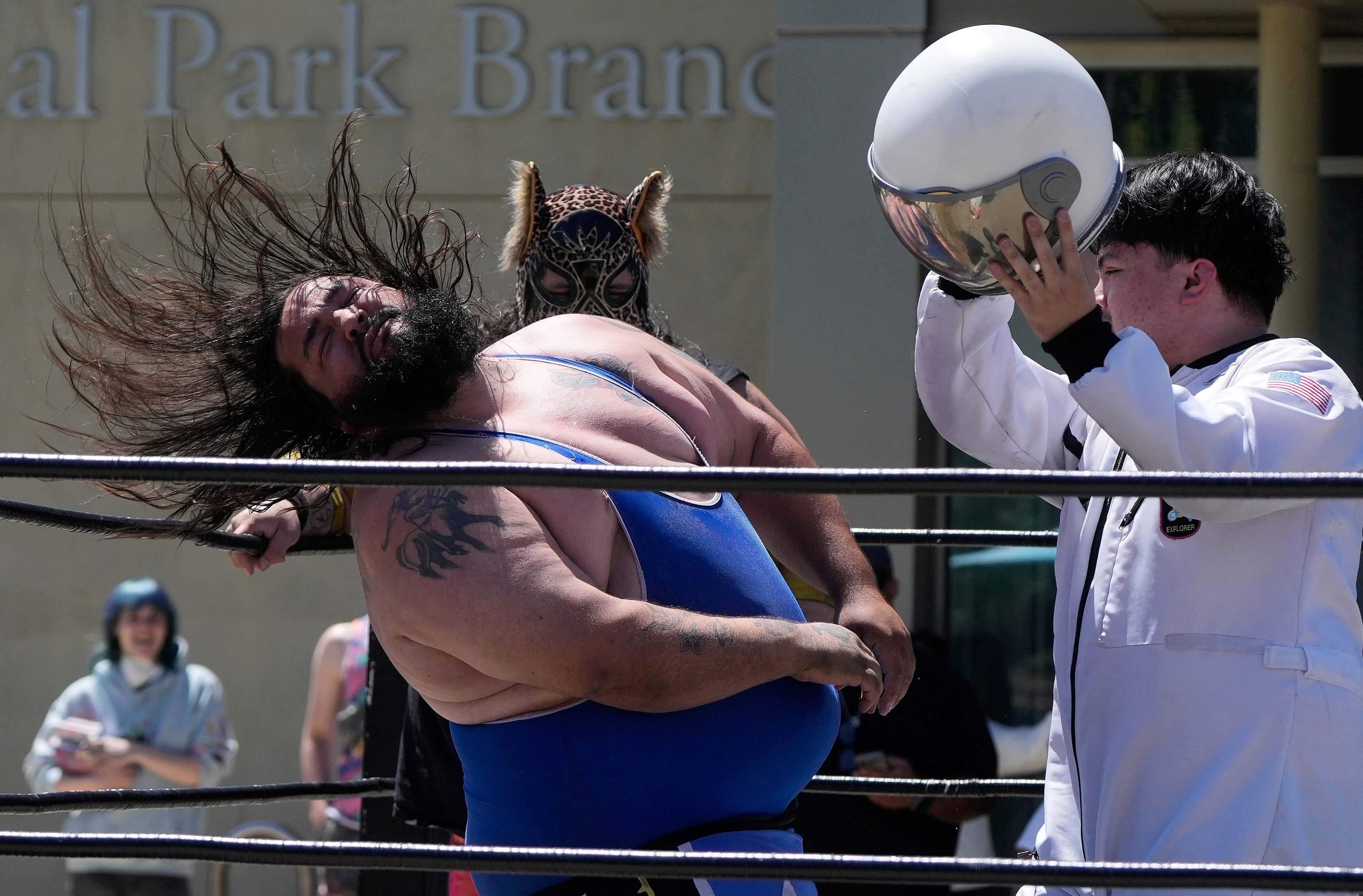 A pro wrestler flings his head back after being struck by another wrestler holding an astronaut helmet.