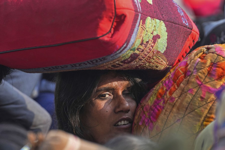 A woman carries luggage on her head in a tightly-packed crowd.