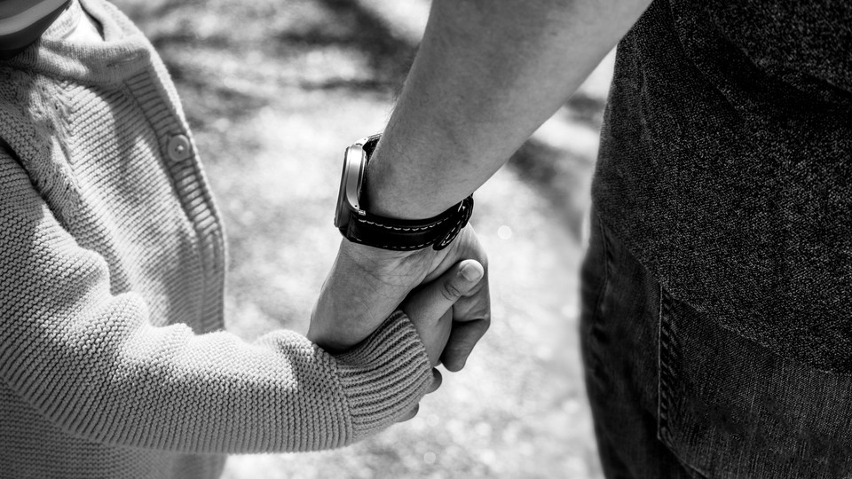 Black-and-white close-up image of an adult hand holding a child's hand