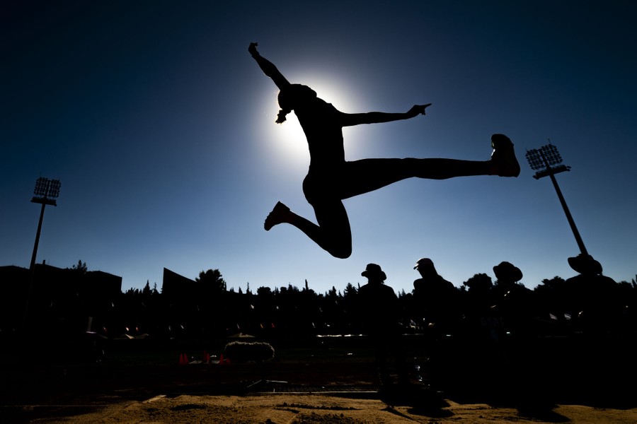 A person leaps in a long-jump competition, captured in silhouette.