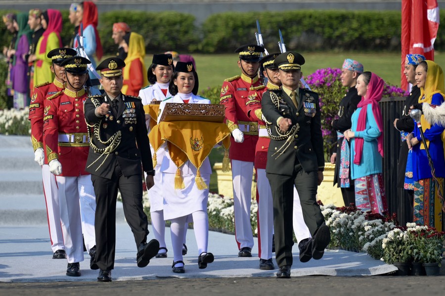Eight members of a squad in dress uniforms carry decorated cases on a path during a ceremony.