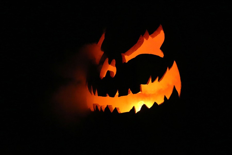 Smoke emanates from a carved pumpkin that is lit from inside.