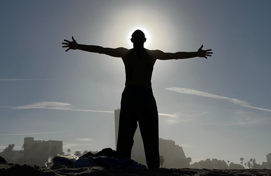 A man stands, arms open wide to the sun overhead.