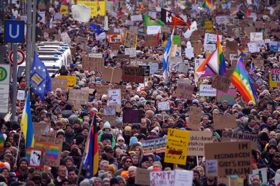 Hundreds of people carry hand-made protest signs and flags.