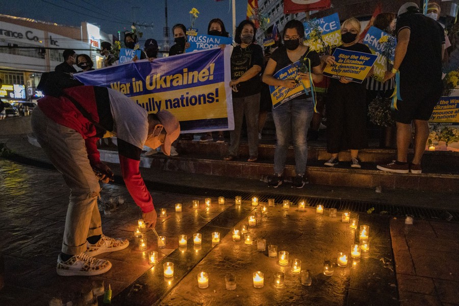 A crowd of protesters stands in a plaza while one lights candles in the shape of a peace symbol.