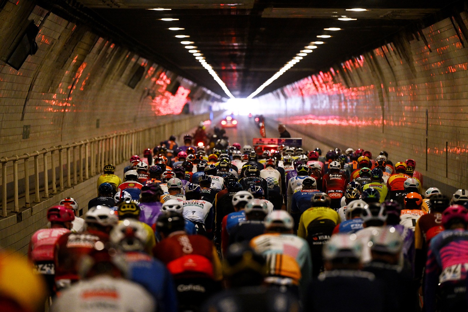 A view from behind of a pack of bicycle racers riding through a road tunnel.