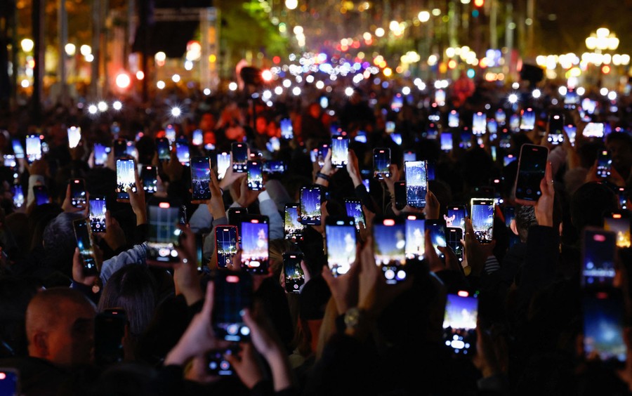 Many people record video with various devices in a crowd in a street.