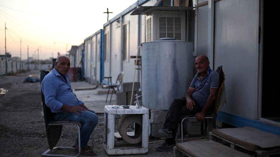 Christian men are seated outside a trailer at the Ankawa refugee camp in Erbil, Iraq, on September 12, 2018.