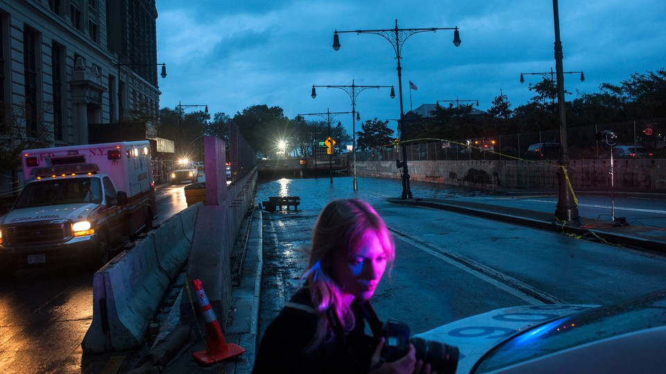 A woman looks at a car next to an ambulance and a flooded tunnel