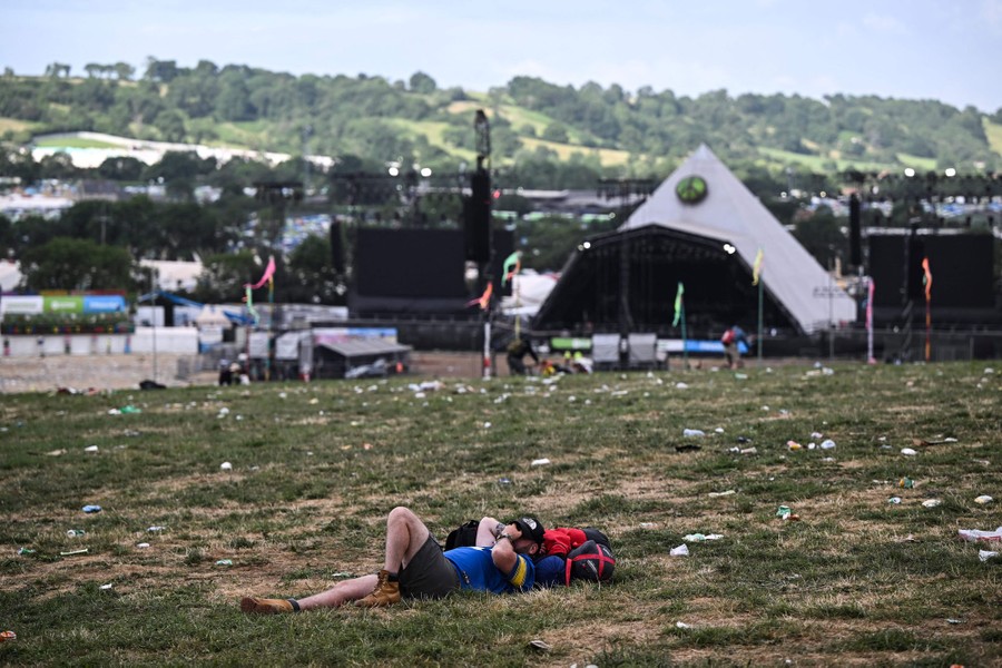 A person lies on the ground in a field strewn with litter, the day after a concert.
