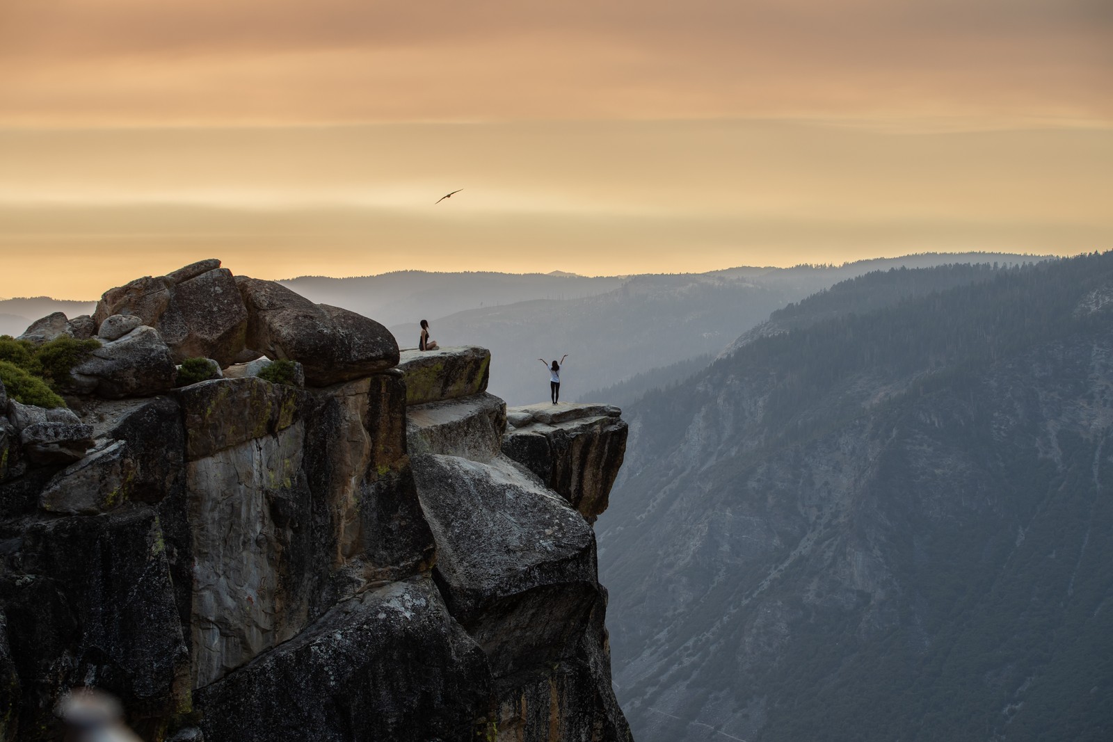 Two people pose for photographs while standing near the edge of a tall cliff in Yosemite National Park.