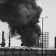 Black and white photograph of smoke rising over an oil refinery in Tehran.
