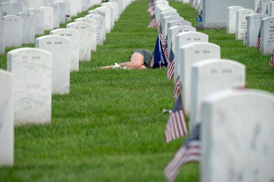A woman lies in front of a grave, her torso obscured by a line of gravestones, in Arlington National Cemetery.
