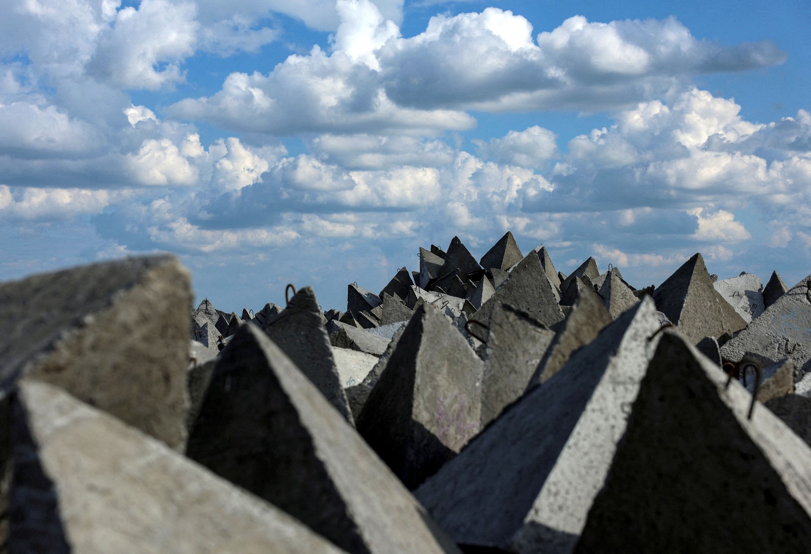 A pile of pyramid-shaped concrete anti-tank fortifications, seen beneath a cloudy sky