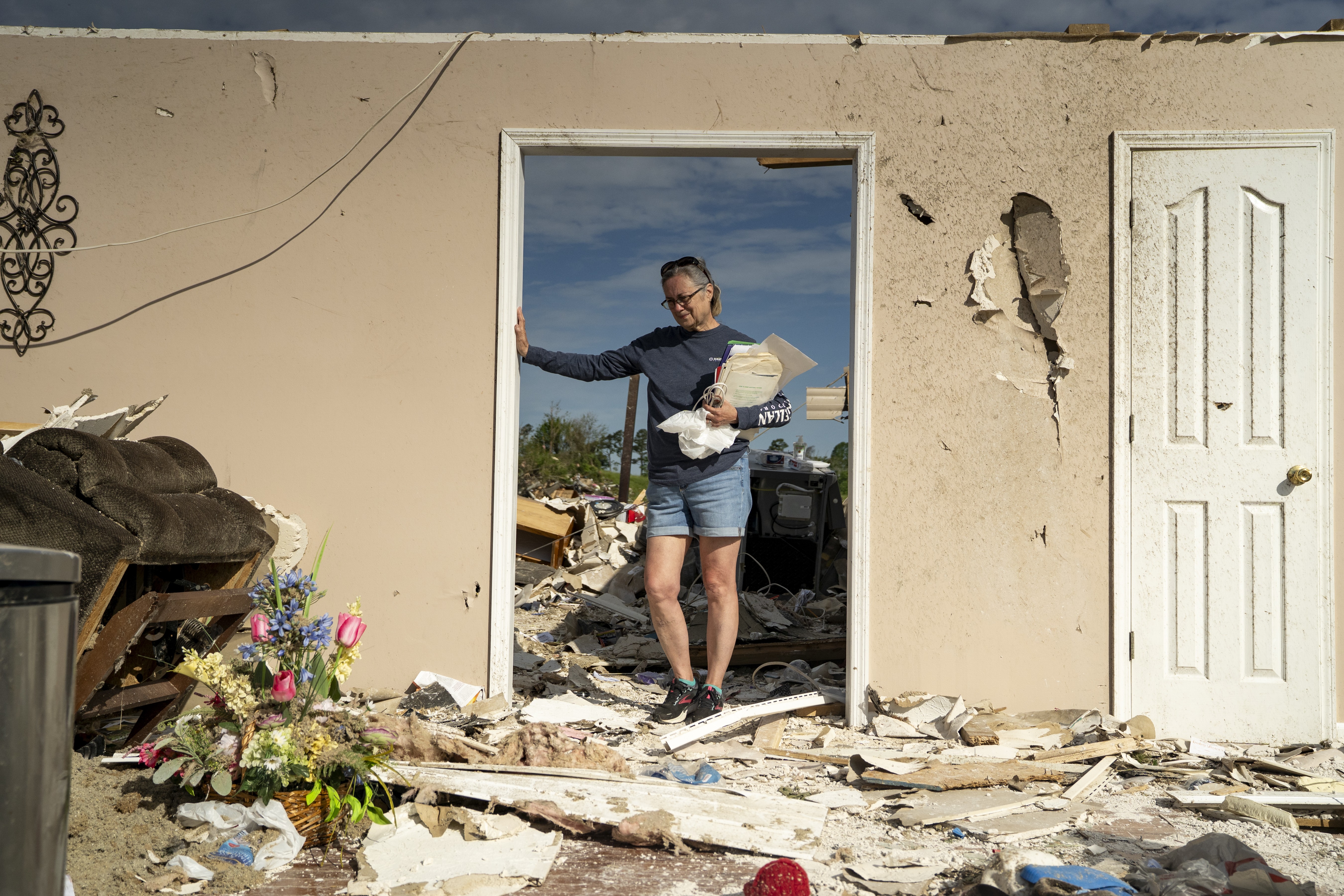 A woman stands in a doorway in her storm-damaged house.
