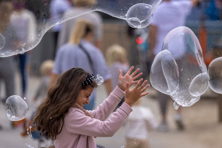 A girl closes her eyes while reaching up toward several large soap bubbles in the air around her.