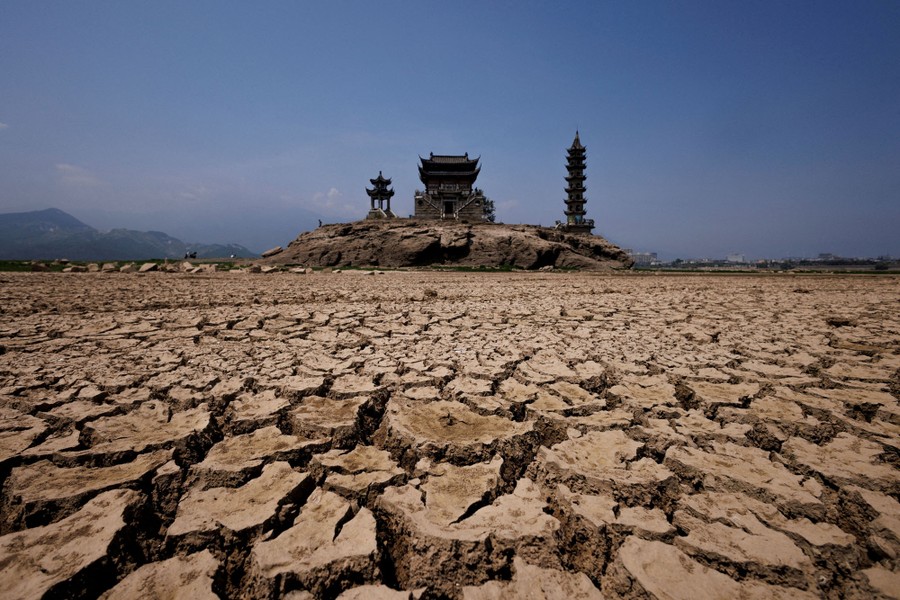 Three pagodas stand atop a rock outcrop, surrounded by cracked, dry earth.