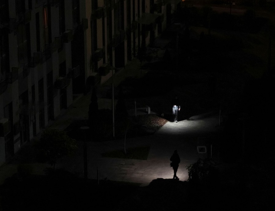 Two people with flashlights walk through a dark apartment courtyard.