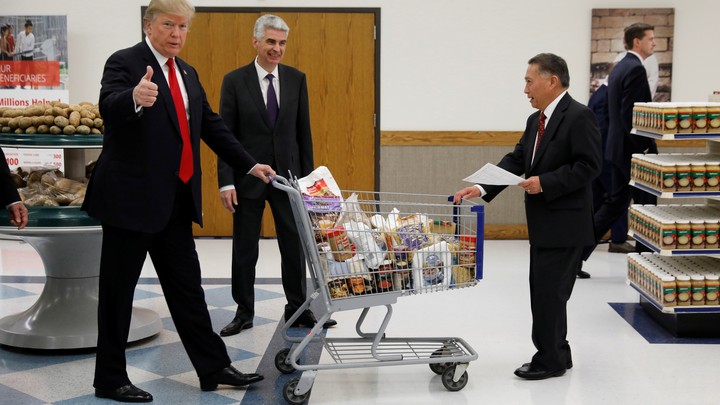 President Donald Trump pushes a shopping cart while giving a thumbs-up.