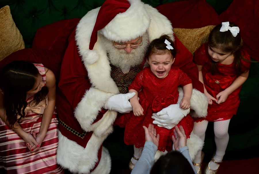 A girl cries while taking photos with Santa Claus.