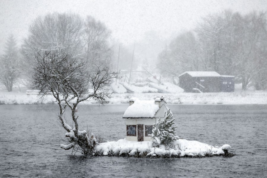 A tiny house on a small lake island, covered in snow.