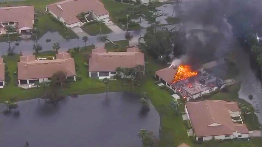 An aerial view of a residential street with one of the houses on fire.