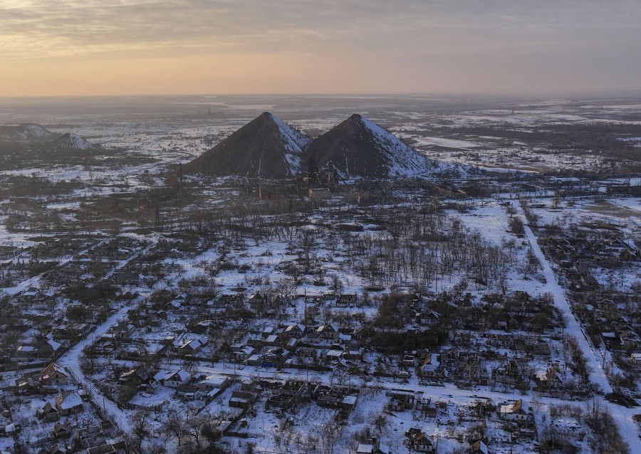 An aerial view of a small war-damaged town, backdropped by two enormous mounds of dirt from a nearby mine