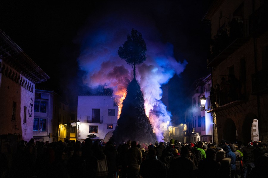 A crowd of people gather in a square to watch a large bonfire burn.