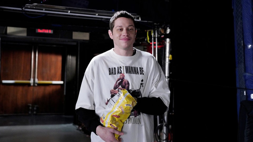 Pete Davidson holding a bag of chips in the SNL studio