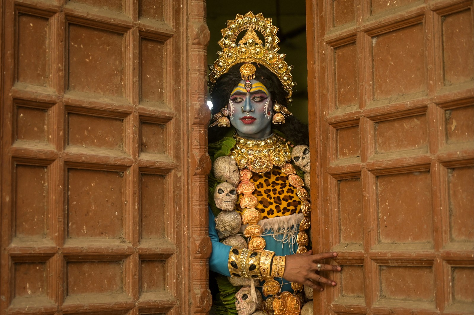 A person dressed as the Hindu goddess Kali waits inside a doorway.