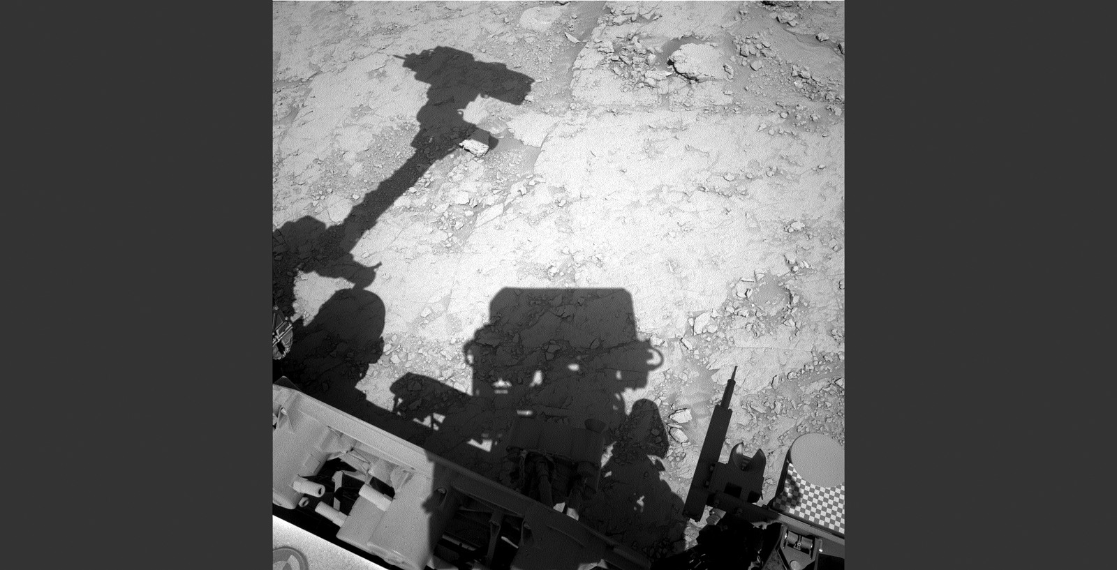 A shadow is cast by a Mars rover, seen on rocky ground.