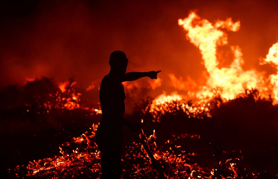 A firefighter points as he stands near flames.